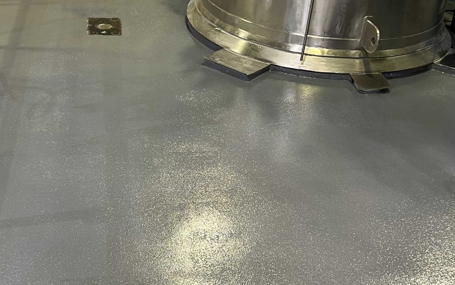 Seamless textured resinous floor detailed tight to the base of a stainless steel process vessel