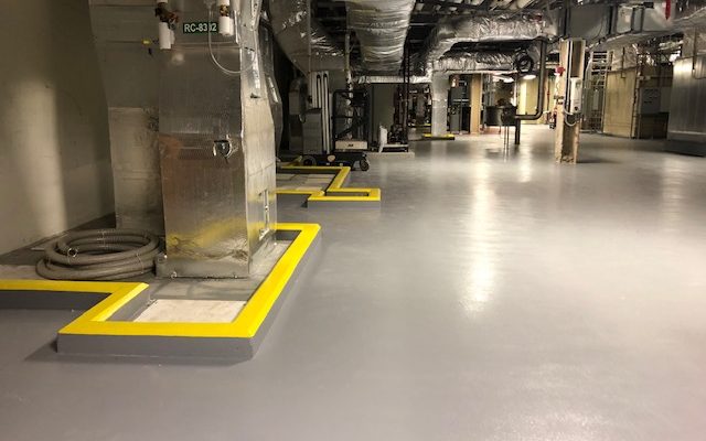 Mechanical equipment room with seamless gray floor and yellow demarcation borders around equipment pads