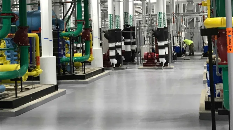 Gray epoxy floor through a central utility plant mechanical room with chilled-water pumps and piping